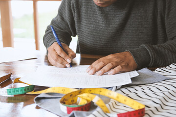 A young man fashion designer writing on paperwork, on messy desk.