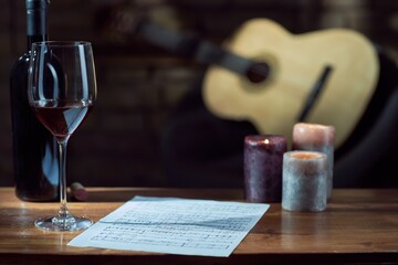 Fototapeta na wymiar Music notes, wine, candle on wooden table, with a guitar in the background.