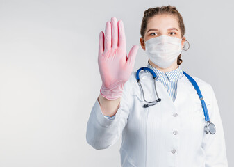 Young woman doctor shows stop gesture on white background. Say No virus disease. Copy space