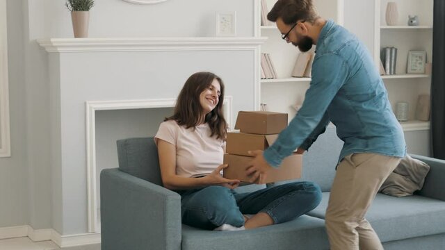 Happy funny man giving gift boxes with toilet paper to beautiful young woman at home. Happy thankful female smiling laughing. Funny gift and surprise for birthday. Funny wife and husband