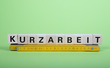 Holzklötze bilden das Wort Kurzarbeit, darunter liegt ein Zollstock