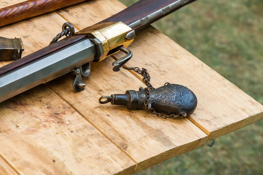 old flintlock shotgun close-up, with an iron vessel a powder flask on chains