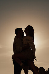 Young tourist couple in the setting sun against the backdrop of a sky. The couple hugging and having fun. Dark silhouette. Copy space.