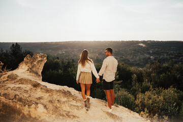 Beautiful stylish young couple in love walking in the summer on the mountain. They standing together on top of mountain. Lovely couple reached top of stone rock, feel happy see beautiful view. 