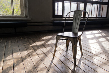 In a bright, empty room with large Windows, there is a wooden chair with metal legs and a back. Pleasant light from the sun through the Windows, soft shadows on the floor