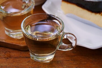 Gray wormwood herbal tea in a glass cup, dry sagebrush flowers in spoon, fresh flowers in a mortar and on table against dark wooden board