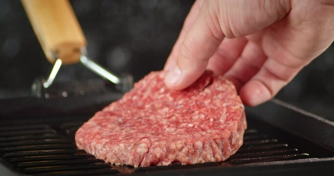 The men's hand puts raw burger meat in a pan for cooking.