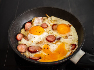 Breakfast - scrambled eggs with sausages and  vegetables in frying pan
