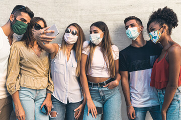 A multiracial group of young people have fun taking selfies with their smartphones together wearing the protective mask against the coronavirus. A concept of new behavioral habits and normality