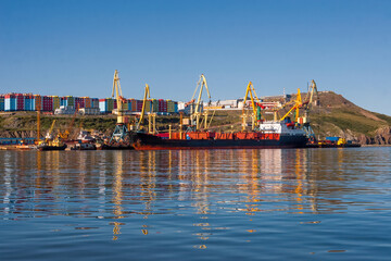 Fototapeta na wymiar View of the seaport located in the Far North in the Arctic. Cargo ship near the pier. Large port cranes on the terminal harbour. Shipping and stevedoring services. Anadyr, Chukotka, Far East of Russia