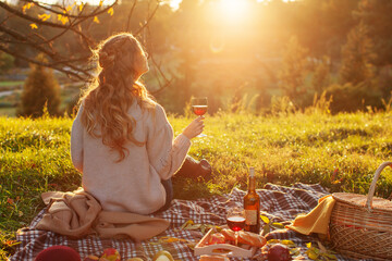 Girl Autumn Picnic. Perfect autumn warm day, autumn picnic in nature. girl sitting on a plaid with a wicker basket of products and a bottle of young red wine is enjoying the peace and sunshine 