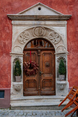 Fototapeta na wymiar Brown old elegant front wooden carved door with a decorative flower wreath, green plants in a pot, red wall. Cesky Krumlov, South Bohemia, Czech Republic