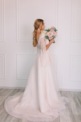 Fototapeta premium young woman in a white wedding dress with long hair before the engagement ceremony with a bouquet of flowers on a white background with a model appearance important wife for the bride 