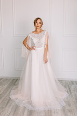 Fototapeta premium young woman in a white wedding dress with long hair before the engagement ceremony on a white background with a model appearance important wife for the bride posing in front of the photographer 