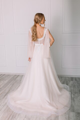 Fototapeta premium young woman in a white wedding dress with long hair before the engagement ceremony on a white background with a model appearance important wife for the bride posing in front of the photographer 
