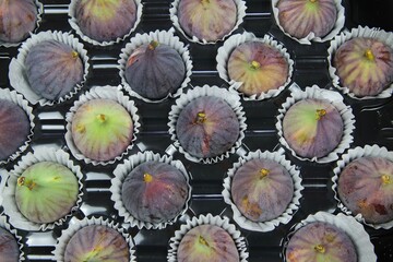 High angle view on isolated fresh ripe figs in paper cupcakes cups on black plastic tray