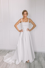 Fototapeta premium young woman in a white wedding dress with long hair before the engagement ceremony on a white background with a model appearance important wife for the bride posing in front of the photographer 