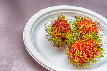rambutan pink hairy asia fruit lies on a plate close-up