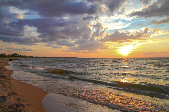 Sunset Beach. Waves crash on a sandy beach with a sunset horizon on the coast of the Great Lakes on a warm summer night.