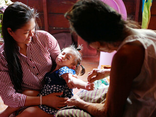 Thai mother carrying her baby girl, while allowing her grandmother to do a blessing for the toddler...