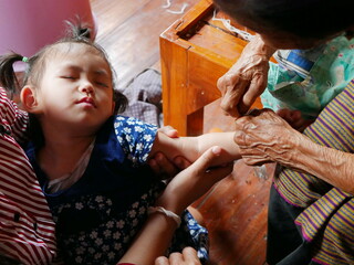 A Thai baby girl falling asleep, while her great grandmother doing a blessing for her by waving a...