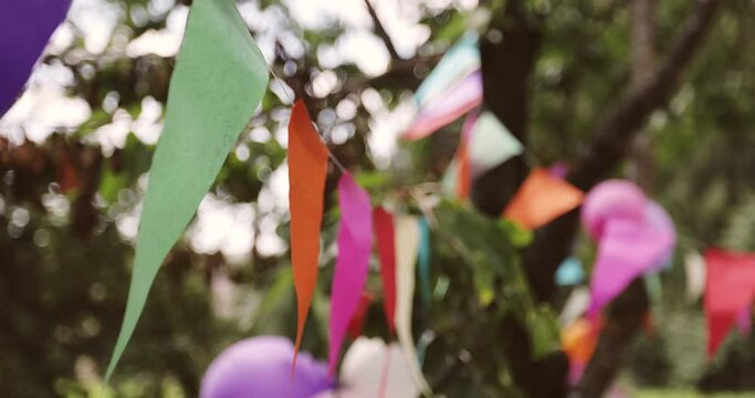 Colorful flags hanging on branches of trees as festive decoration for outdoor party. Outdoor decoration.