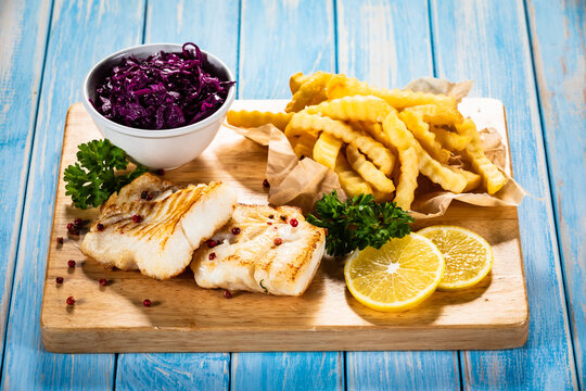 Fish dish - fried cod fillet with curly french fries and vegetable salad on wooden table
