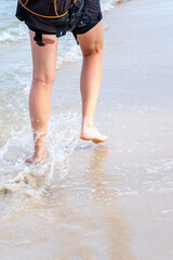 girl walks along the sandy beach of the ocean, legs in the water