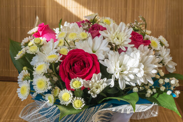 A festive bouquet of different and bright flowers stands at the window on a bamboo napkin