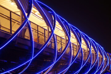 A view of the cityscape at night with a pedestrian bridge and high buildings, people walk inside...