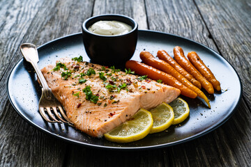 Fried salmon fillet with carrots, lemon and cream sauce served on black plate on wooden table
