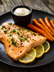 Fried salmon fillet with carrots, lemon and cream sauce served on black plate on wooden table 
