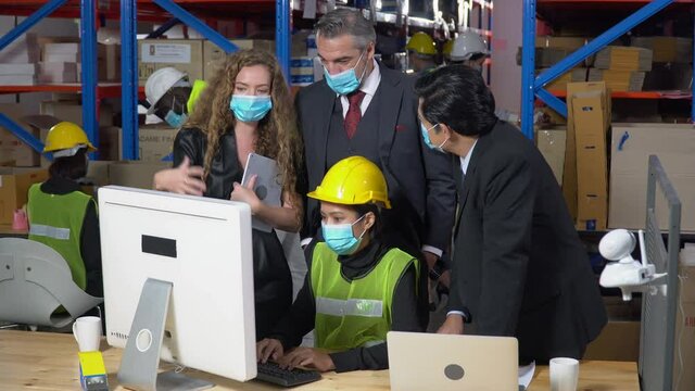 Executive business man and secretary woman wearing face protective medical mask talking to asian warehouse manager and looking to computer and laptop in large warehouse