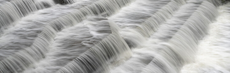 Fototapeta na wymiar White Water flowing over weir low-level view at long exposure to give blurred motion effects