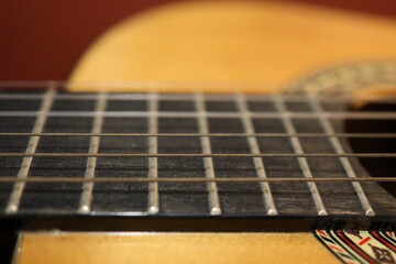 Fototapeta premium Saiten einer orangenen klassischen Gitarre mit einem schönverzierten Korpus aus der Nähe mit einem Marko Objektiv fotografiert. Es ist ein roter Hintergrund zu sehen.