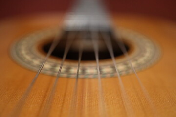 Fototapeta premium Saiten einer orangenen klassischen Gitarre mit einem schönverzierten Korpus aus der Nähe mit einem Marko Objektiv fotografiert. Es ist ein roter Hintergrund zu sehen.