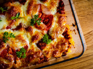 Pasta casserole with minced meat, mozzarella cheese and vegetables on wooden table
