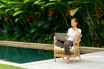 Young woman near blue swimming pool and working freelance at latop computer