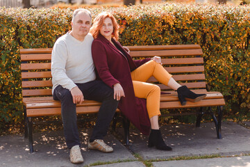man and woman of fifty years sit on a park bench in the fall while the counter light
