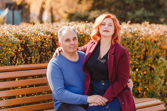 A red-haired woman sits on the lap of a five-year-old man on a park bench in the fall - Powered by Adobe