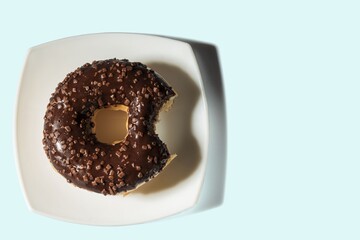 Close up view of bitten donut on white plate isolated on blue background.  Food and health concept.