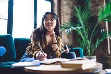 Young ethnic lady writing in notebook in modern workspace