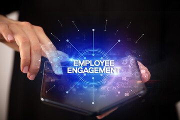 Fototapeta premium Businessman holding a foldable smartphone with EMPLOYEE ENGAGEMENT inscription, new business concept