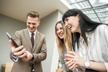 A guy is showing something on his tablet to a two girls. They are laughing together
