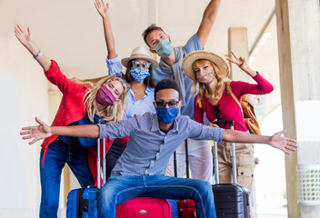 Multiracial group of friends at train station with luggage wearing protective mask. Tourism and...