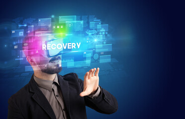 Businessman looking through Virtual Reality glasses with RECOVERY inscription, innovative security concept