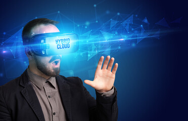 Businessman looking through Virtual Reality glasses with HYBRID CLOUD inscription, cyber security concept