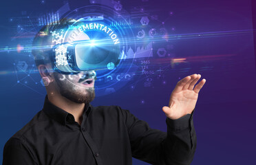 Businessman looking through Virtual Reality glasses with IMPLEMENTATION inscription, innovative technology concept