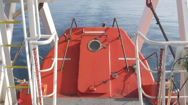 View from the stern of an orange freefall lifeboat aft of an oil tanker.