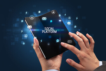 Businessman holding a foldable smartphone with SOCIAL PLATFORM inscription, social networking concept